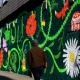 Image shows the Reid Lane mural grafitti with a community garden theme. The artwork contains local community garden flowers and many animals including snails, birds, ladybirds and cats. Mural by Ida Henrich