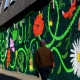 Image shows the Reid Lane mural graffiti with a community garden theme. The artwork contains local community garden flowers and many animals including snails, birds, ladybirds and cats. Mural by Ida Henrich