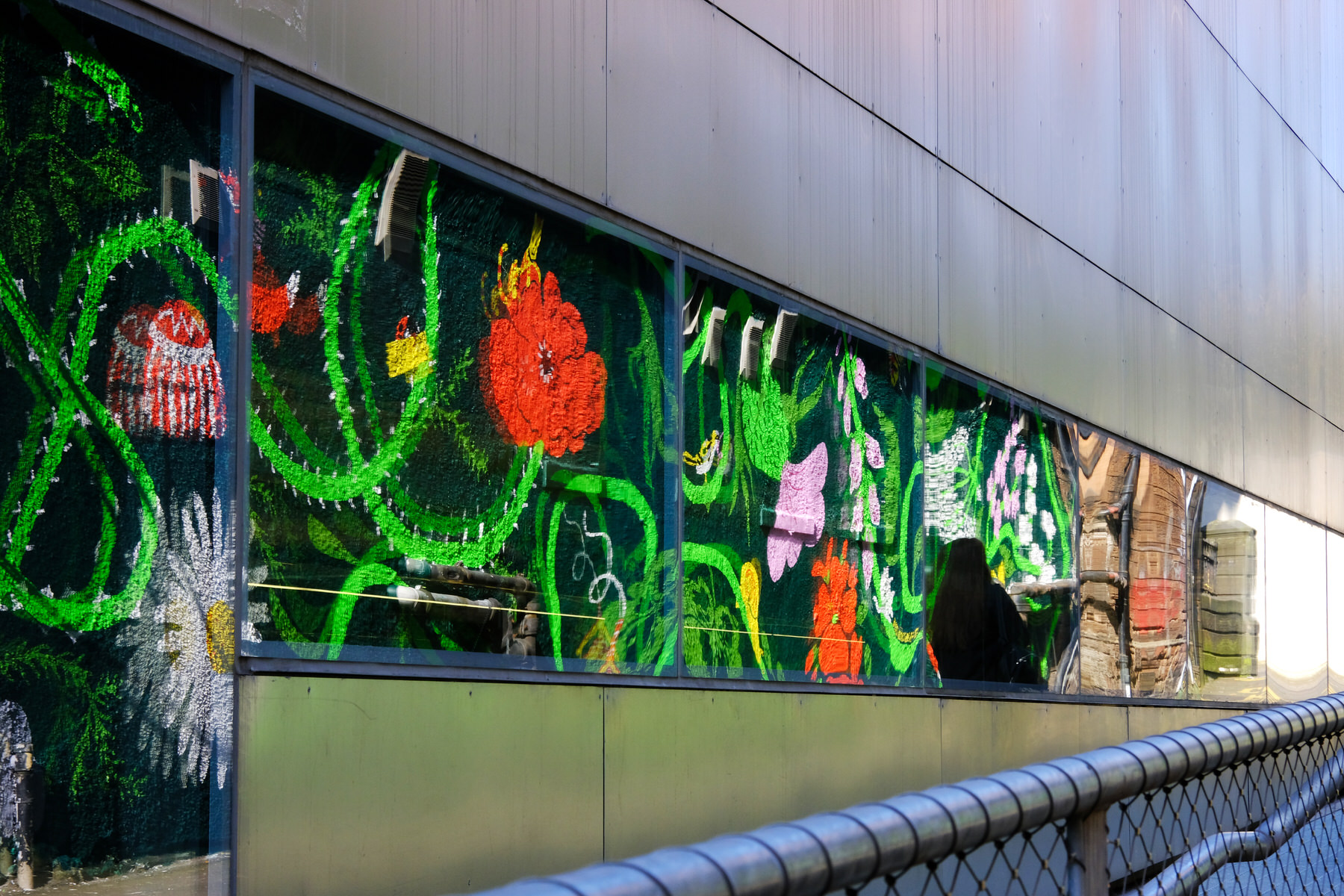 Image shows the Reid Lane mural with a community garden theme. The artwork contains local community garden flowers and many animals including snails, birds, ladybirds and cats. Mural by Ida Henrich